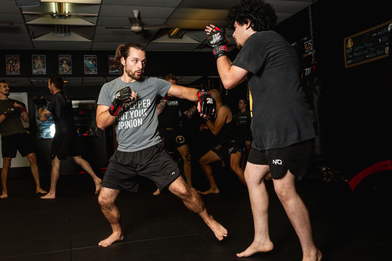 Two men sparring in a martial arts gym, wearing protective gloves.
